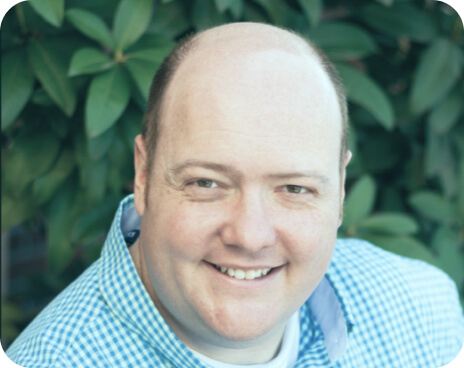 smiling bald man wearing blue plaid shirt outdoors