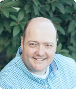 smiling bald man wearing blue plaid shirt outdoors
