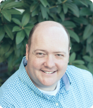 smiling bald man wearing blue plaid shirt outdoors