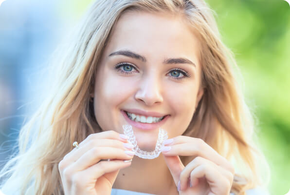 beautiful blonde woman holding invisalign clear aligner
