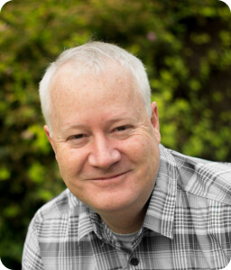 older man wearing grey plaid smiling outdoors