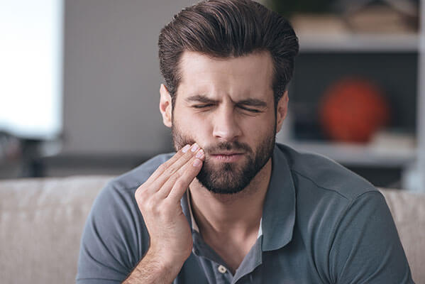 brunette man holding side of cheek in pain