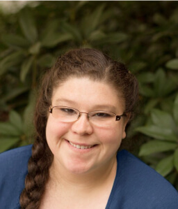 brunette woman with glasses smiling against trees