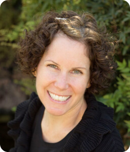 smiling woman with short curly hair against trees