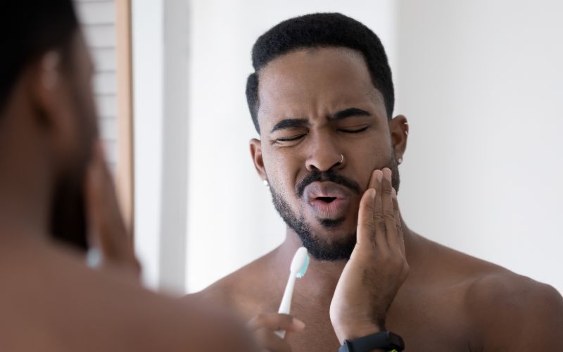 man who's holding his jaw in pain with one hand and a tooth brush in another