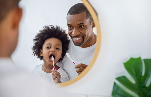 father teaching his son how to brush his teeth