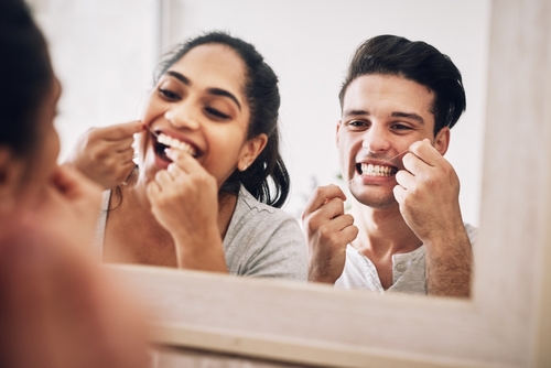 man and woman flossing in mirror