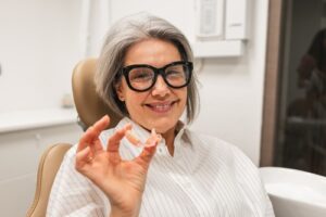 Smiling,Senior,Woman,Receiving,Dental,Care,,Holding,Partial,Dentures,